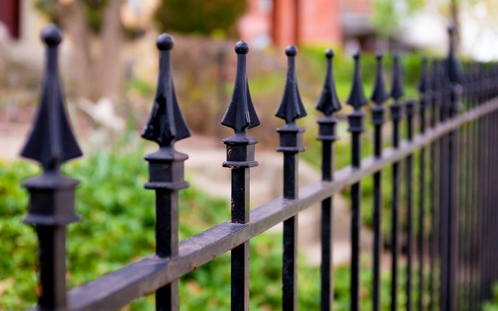 Black metal fence with spear-top pickets beside a garden