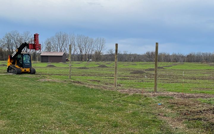 New fence posts set in a line across a field, with a skid steer working at the far end