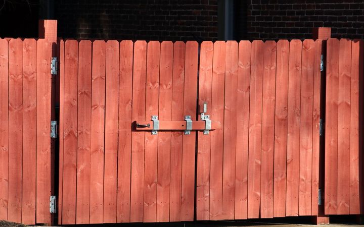 Red board double gate with a slide bolt latch set into a wood fence