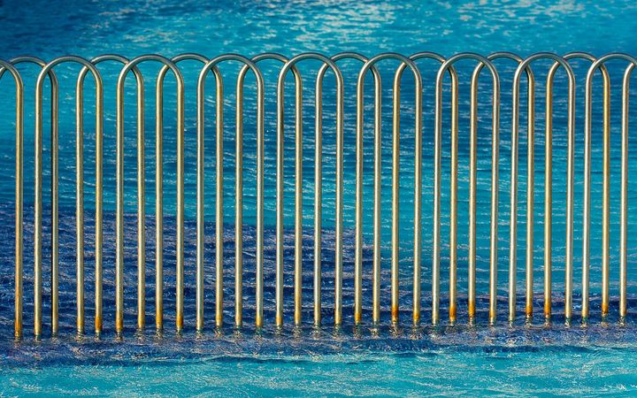 Curved metal barrier fence at the edge of a blue swimming pool